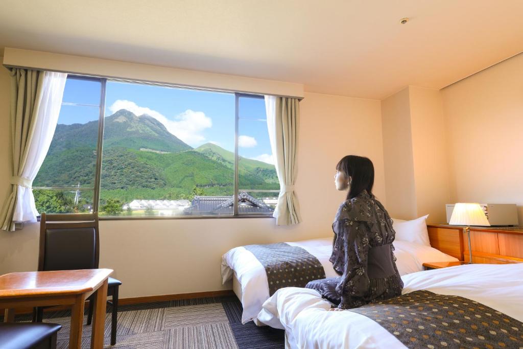une femme assise sur un lit donnant sur une fenêtre dans l'établissement Yufuin Hotel Shuhokan, à Yufu