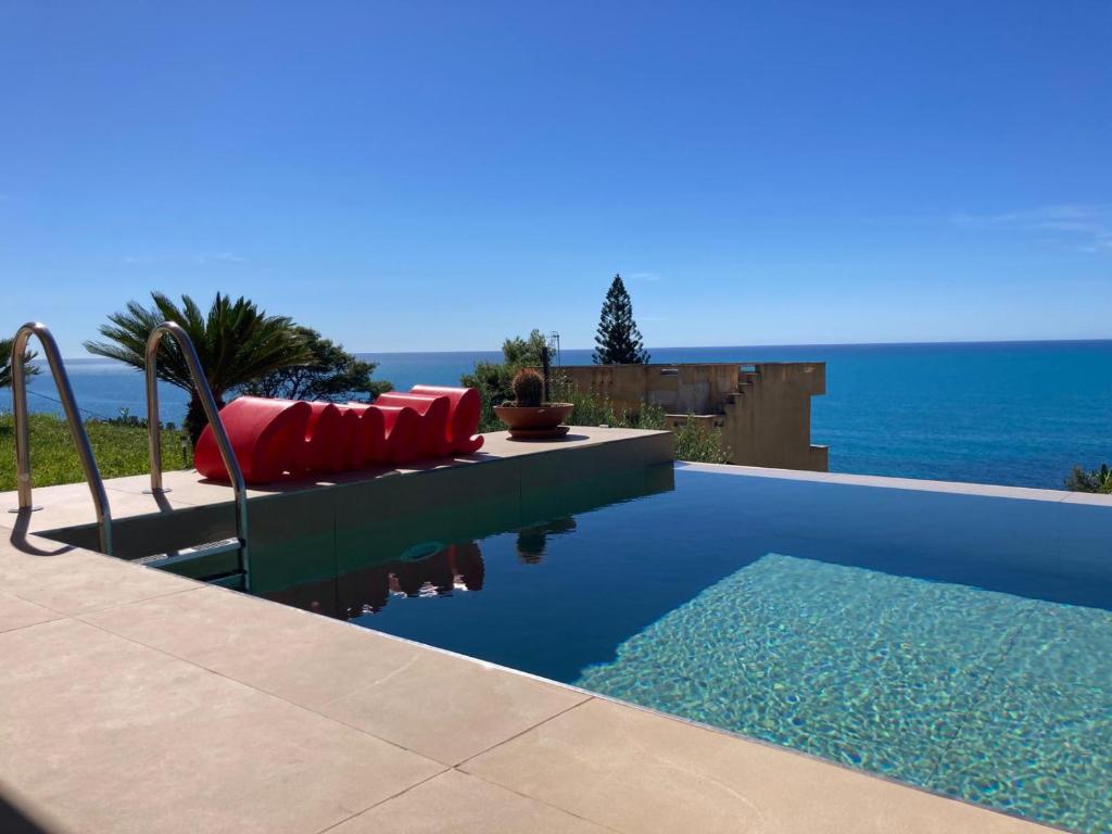 - une piscine avec un canapé rouge et l'océan dans l'établissement Villa Mulberry, à Sciacca