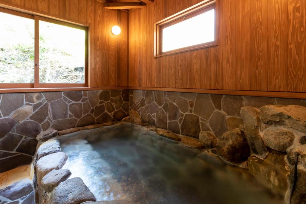 un bain à remous dans une pièce avec un mur en pierre et des fenêtres dans l'établissement Natural Hot Spring Inn Choseian - 長生庵 -, à Shirahama 21 autres photos