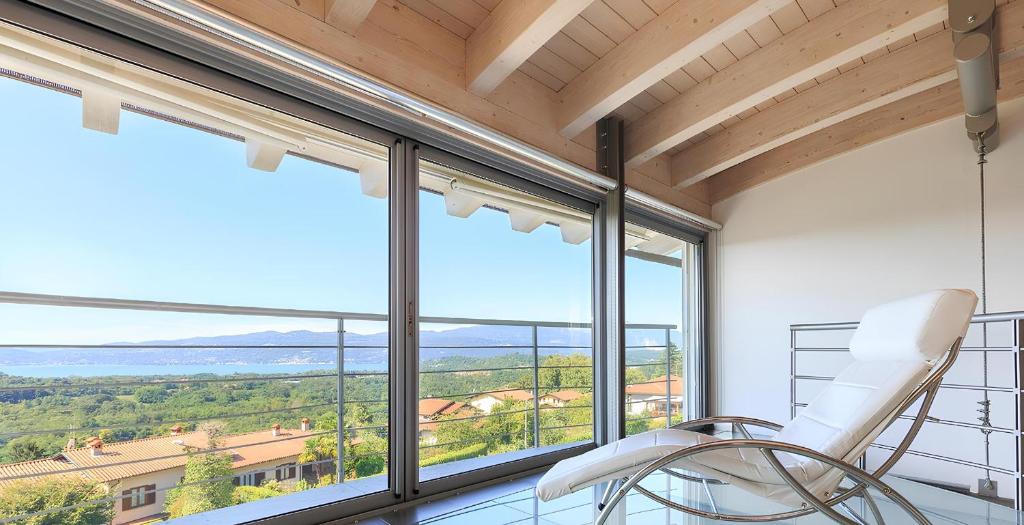 une chaise blanche dans une pièce avec de grandes fenêtres dans l'établissement Villa Panoramica Cardana, à Besozzo