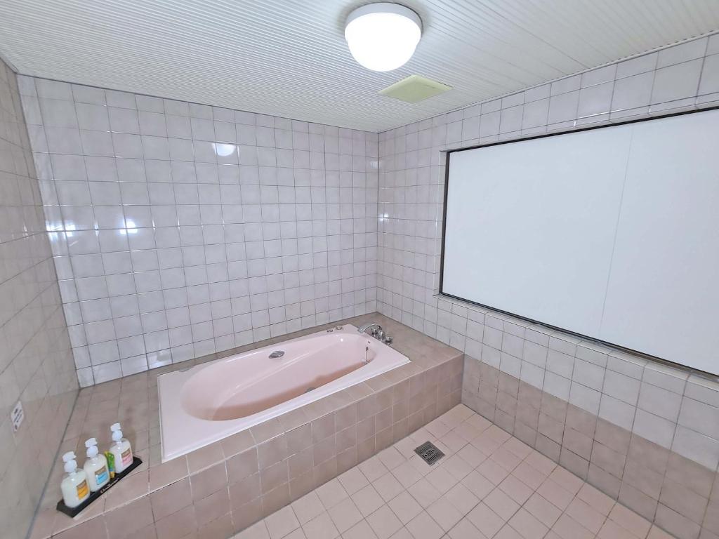 une baignoire dans une salle de bains carrelée avec un grand miroir dans l'établissement Hotel Annex MIE, à Bungoono