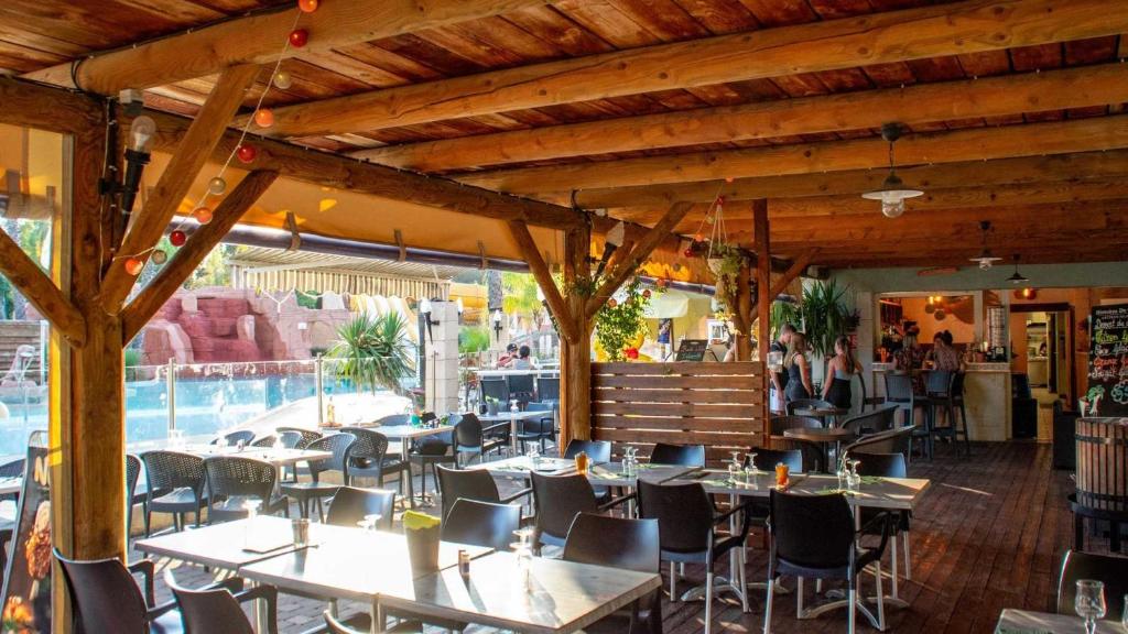 un restaurant avec des tables et des chaises ainsi qu'une piscine dans l'établissement Camping 4 étoiles - Parc aquatique - efacfc, à Hyères