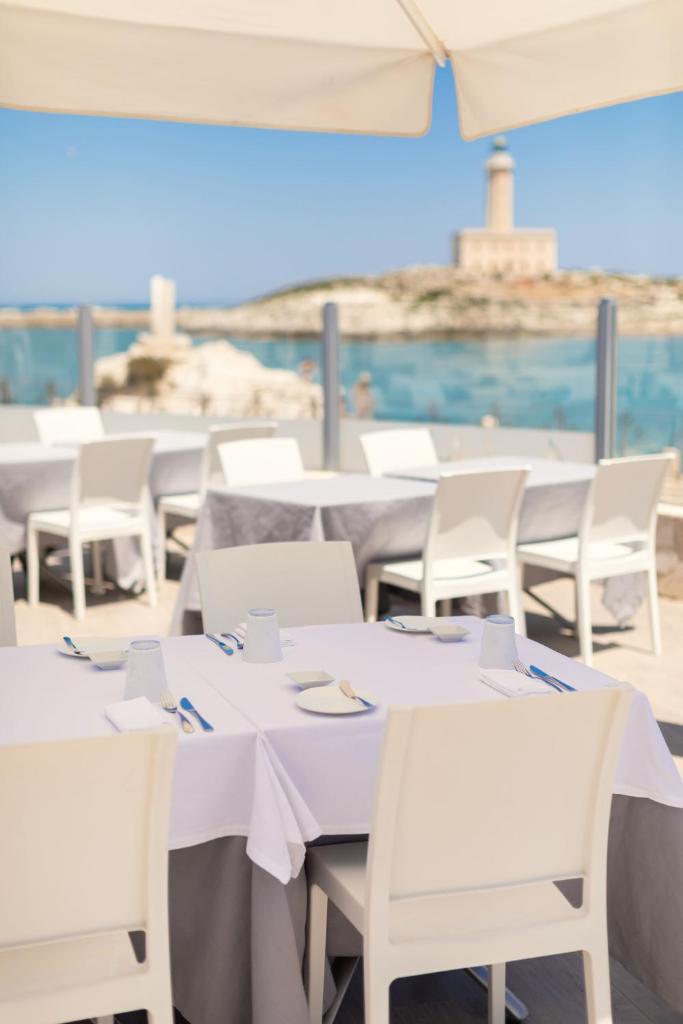 un groupe de tables avec des chaises blanches et un parasol dans l'établissement HOTIDAY Vieste Lungomare, à Vieste