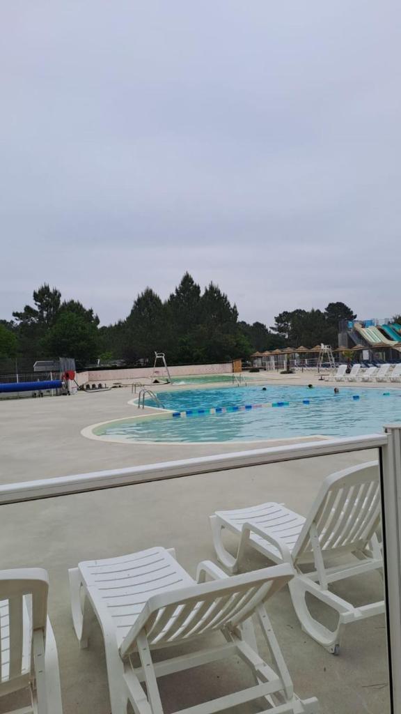 Deux chaises blanches et une piscine en arrière-plan dans l'établissement MH 229 C0C00NING 2ch et 2sdb à proximité des activités dans camping 4 étoiles, à Saint-Julien-en-Born