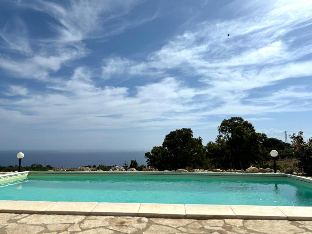 une piscine bleue avec un ciel nuageux dans l'établissement Casale Nocellara, à Scopello