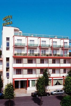 Un grand bâtiment blanc avec un panneau en haut dans l'établissement Hotel Flora, à Lignano Sabbiadoro