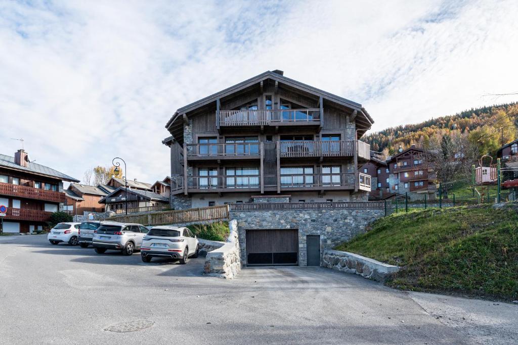 un grand bâtiment avec des voitures garées dans un parking dans l'établissement L'écrin des sapins, à Aime La Plagne