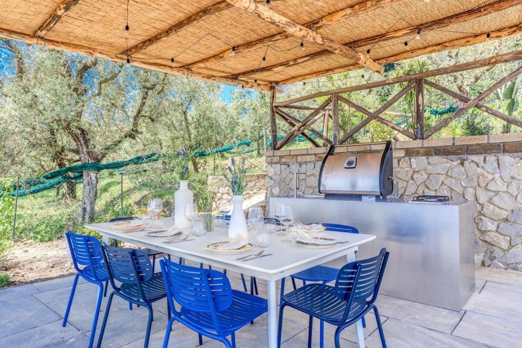 une table blanche avec des chaises bleues et une cuisine dans l'établissement Villa Mediterranea with Heated Pool, Walking Distance from Town by Feeling Italy, à Massa Lubrense