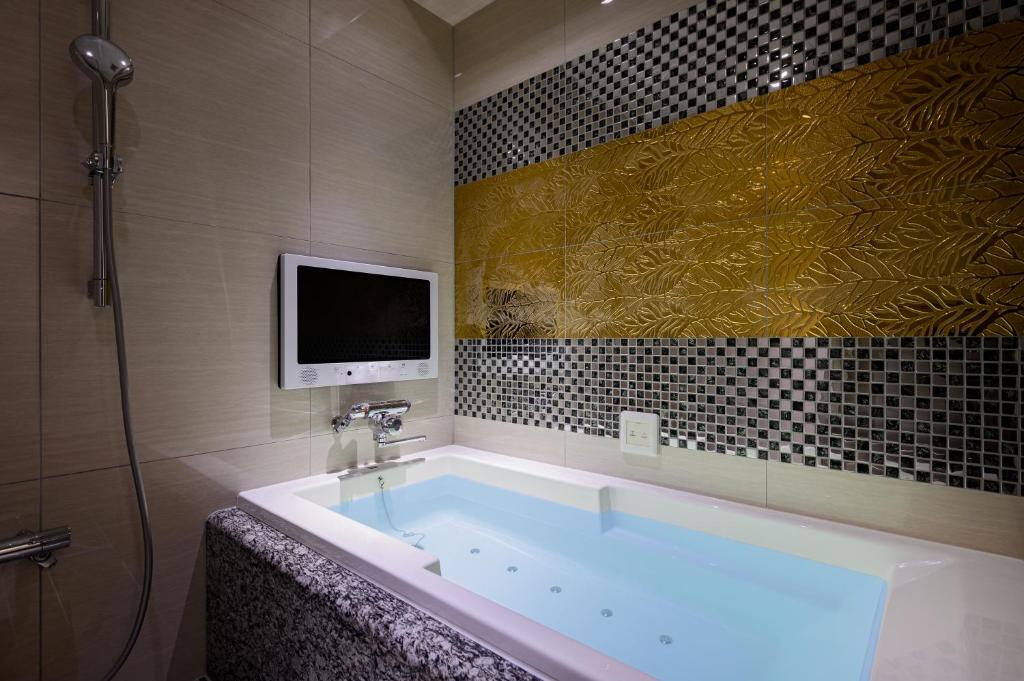 La salle de bains est pourvue d'une baignoire et d'une télévision murale. dans l'établissement ホテルパサディナ富山, à Toyama