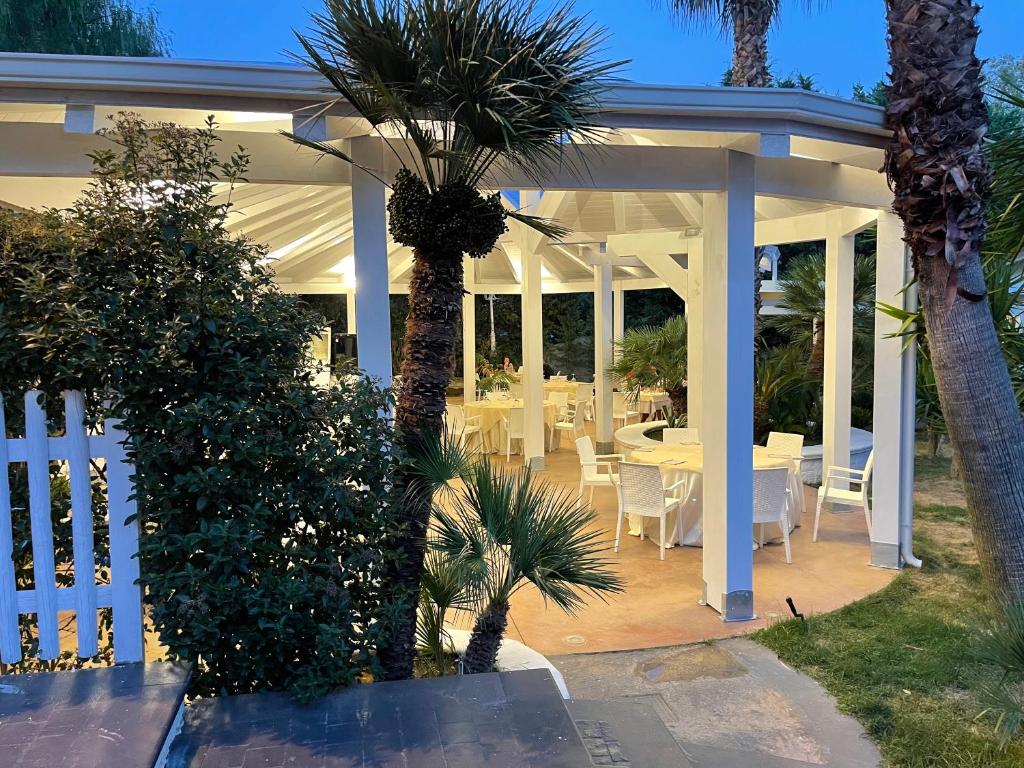 une pergola blanche avec des tables blanches et des palmiers dans l'établissement Hotel Borina by Isola dei sapori, à Foce Varano