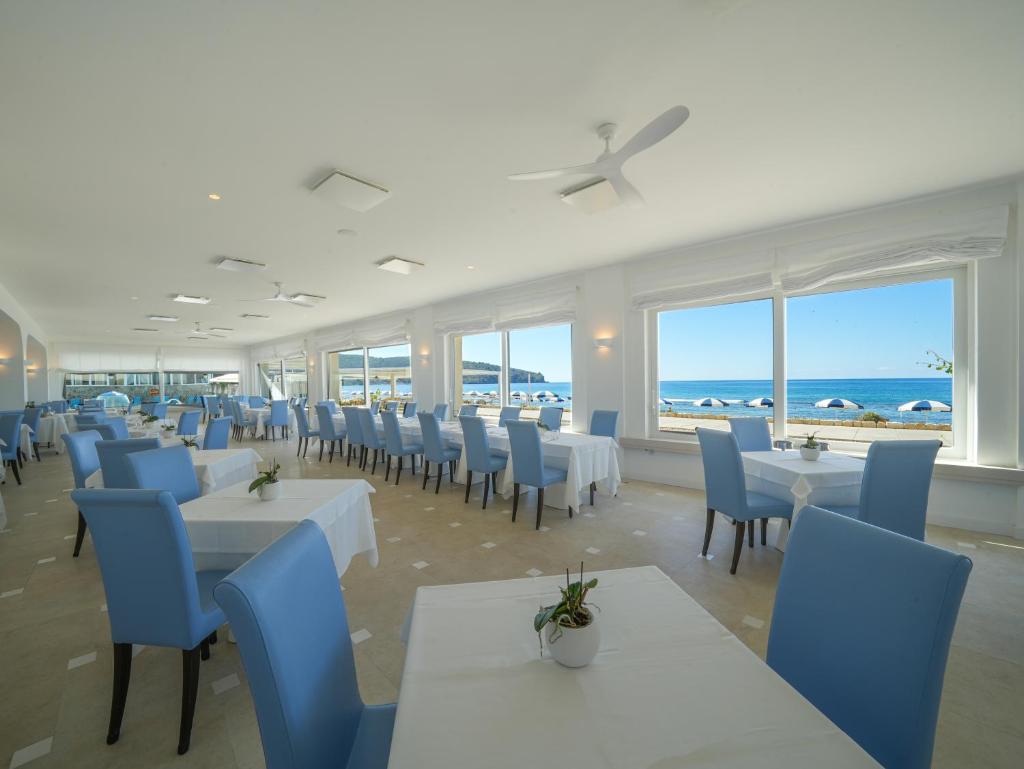 un restaurant avec des tables blanches, des chaises bleues et l'océan dans l'établissement Hotel Saline, à Palinuro