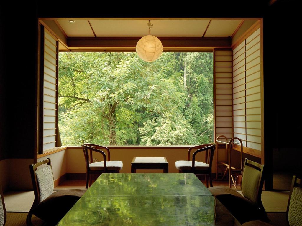 une table et des chaises dans une pièce avec une grande fenêtre dans l'établissement Rankeisou, à Sanjo