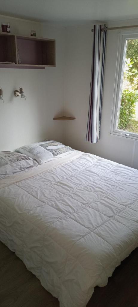 - un lit blanc dans une chambre avec fenêtre dans l'établissement Mobil-home confort dans impasse boisée, à Camiers