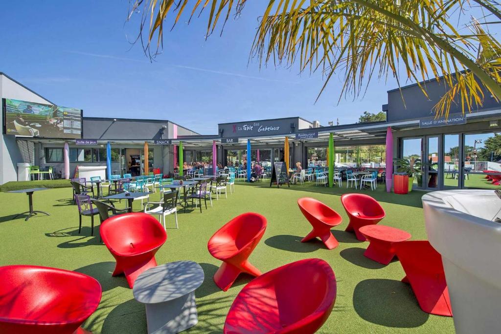 un groupe de chaises et de tables rouges devant un bâtiment dans l'établissement Camping 5 étoiles - Parc aquatique - eeiade, à Brem-sur-Mer