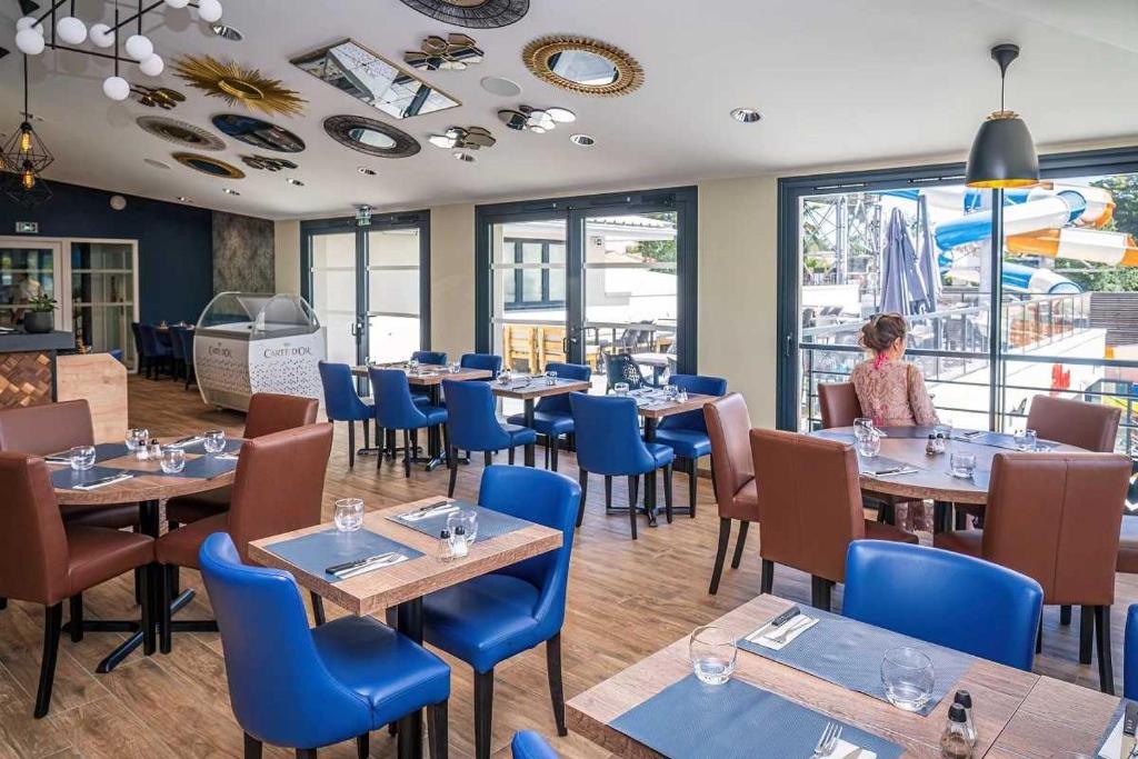 un restaurant avec des tables et des chaises et une femme en arrière-plan dans l'établissement Camping 5 étoiles - Parc aquatique - eei0fd, à Saint-Jean-dʼOrbetiers
