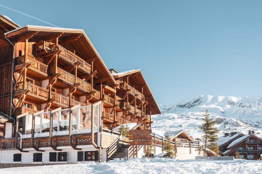 un grand bâtiment en bois dans la neige dans l'établissement Hôtel Au Chamois d'Or by Les Etincelles, à L'Alpe-d'Huez