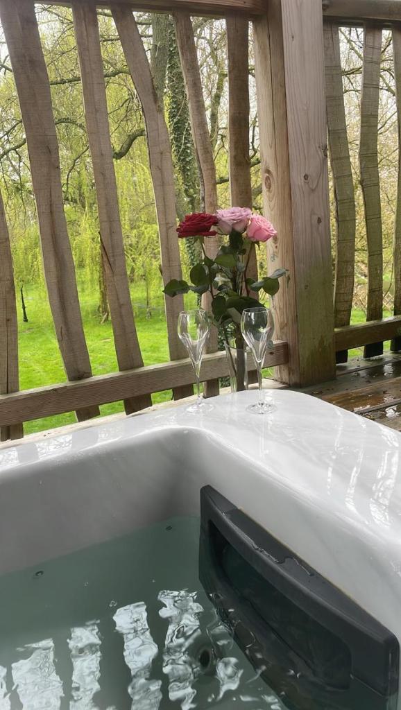 une baignoire avec un vase de fleurs et deux verres à vin dans l'établissement Cabane insolite 2 p Jacuzzi Domaine du Marais 91 Magnolia, à Maisse 3 autres photos