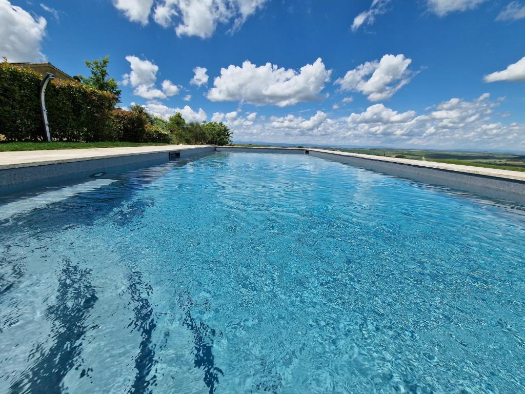 une grande piscine d'eau bleue avec un ciel nuageux dans l'établissement Villa I Cipressini piscina riscaldata spa Toscana, à Pienza