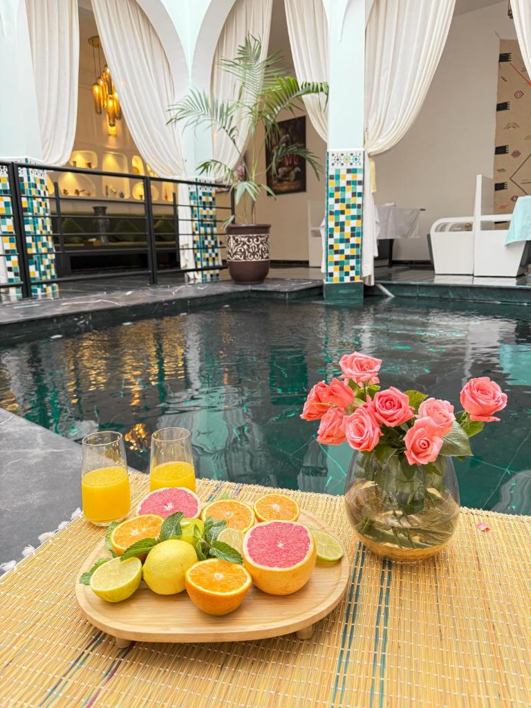 un plateau de fruits et de jus sur une table à côté d'une piscine dans l'établissement Riad L'ECOLE, à Marrakech
