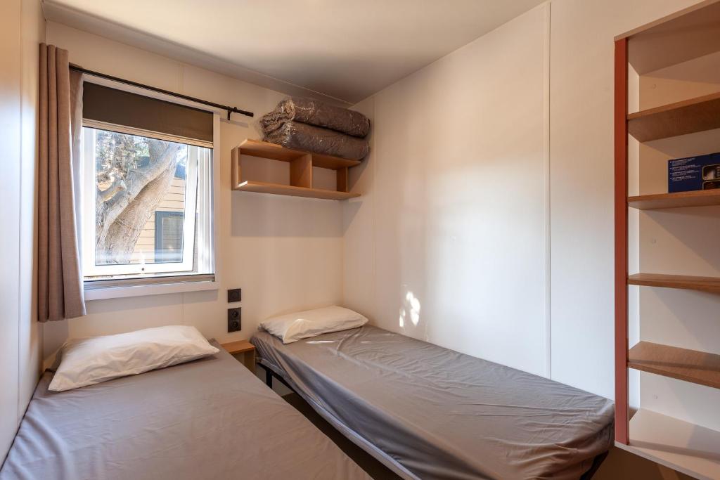 deux lits dans une petite pièce avec une fenêtre dans l'établissement MOBIL HOME Neuf FRONT DE MER TOUT CONFORT 5 LITS 6 personnes CARRY LE ROUET, à Carry-le-Rouet