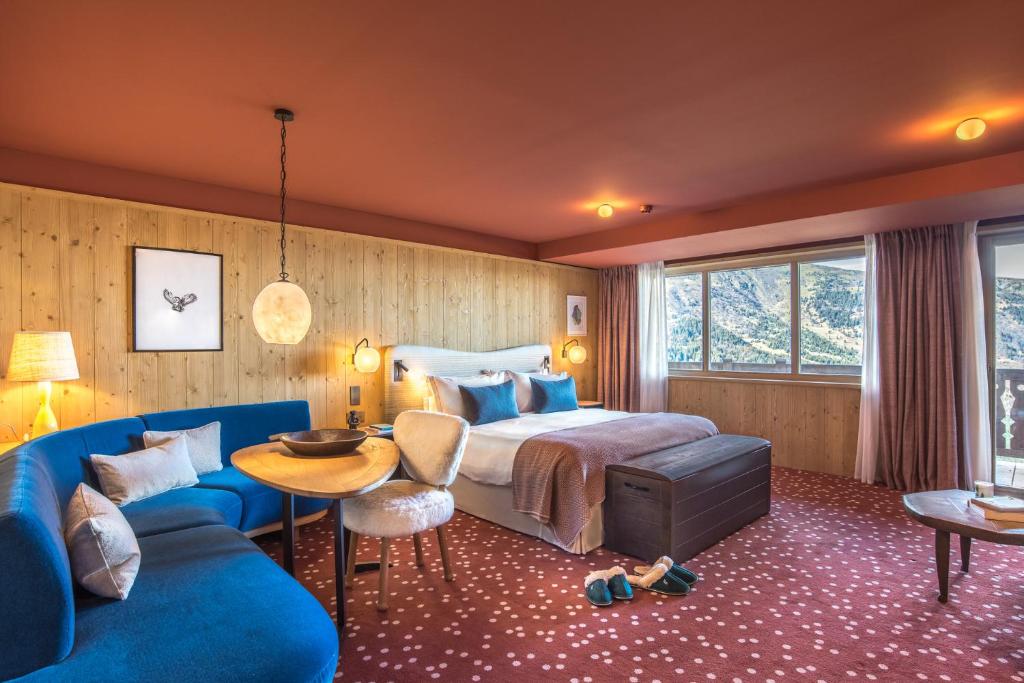 une chambre avec un lit et un canapé bleu dans l'établissement Hotel Le Coucou Méribel, à Méribel