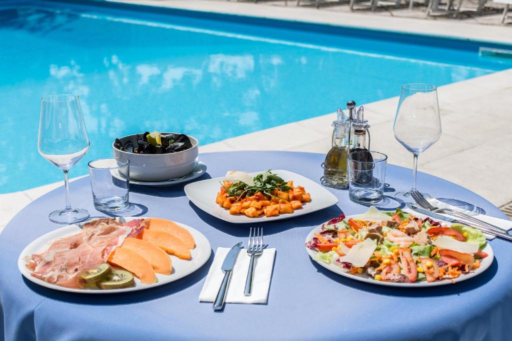 une table avec des assiettes de nourriture sur une table près d'une piscine dans l'établissement Hotel Gioiello, à Cesenatico