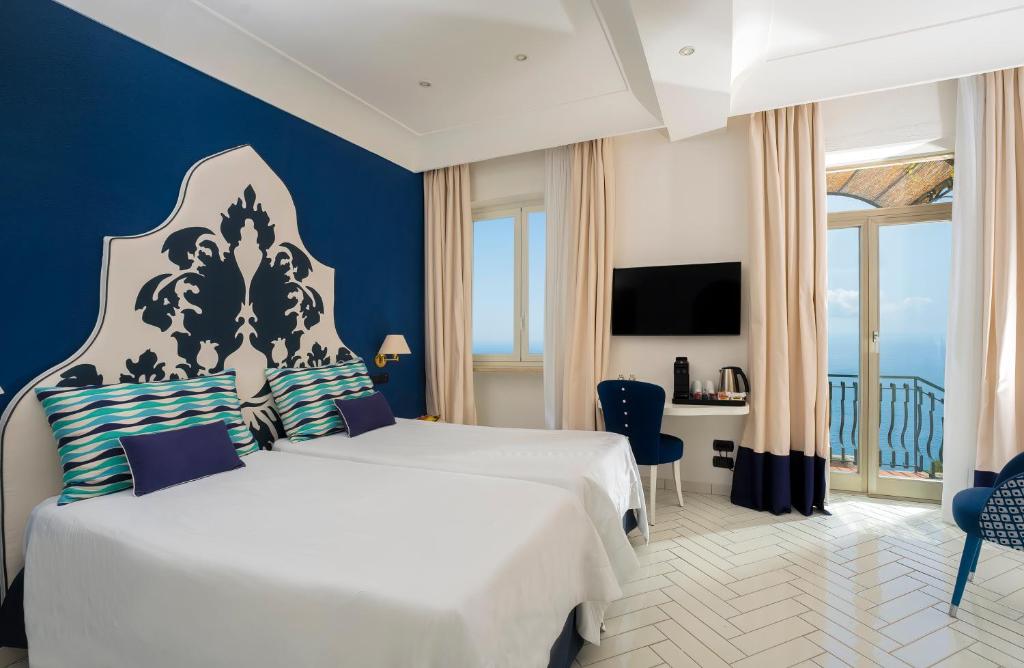 une chambre avec un grand lit blanc et des murs bleus dans l'établissement Hotel Le Agavi, à Positano