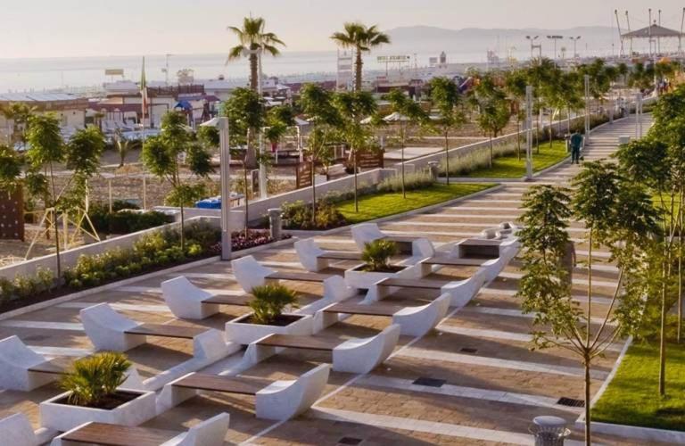 un parc avec des bancs blancs et des palmiers dans l'établissement Hotel Sirius Riccione, à Riccione