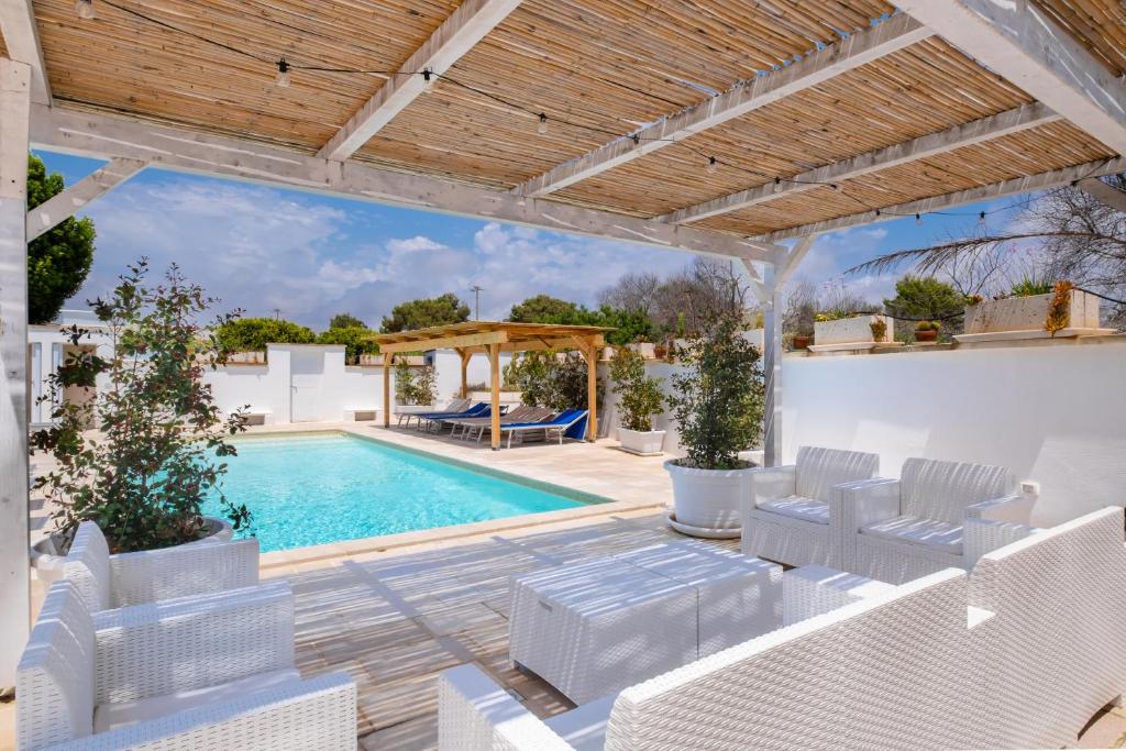 une terrasse avec une piscine et des chaises blanches dans l'établissement Villa Christelle Luxury Pescoluse by HDSalento, à Marina di Pescoluse