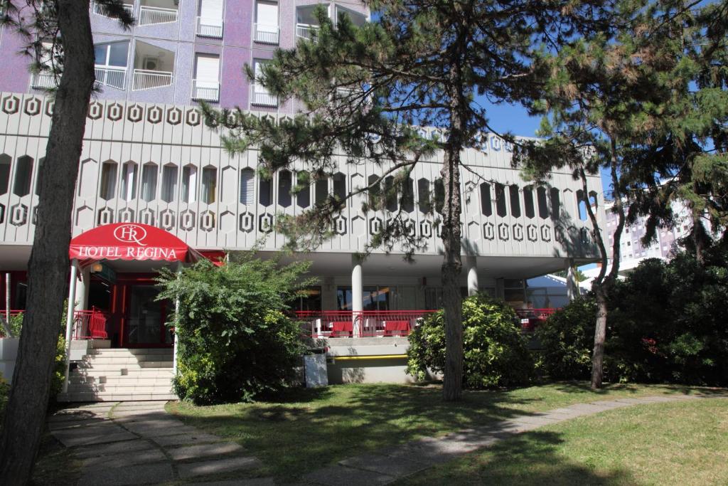 un bâtiment blanc avec des arbres devant dans l'établissement Hotel Regina, à Lignano Sabbiadoro