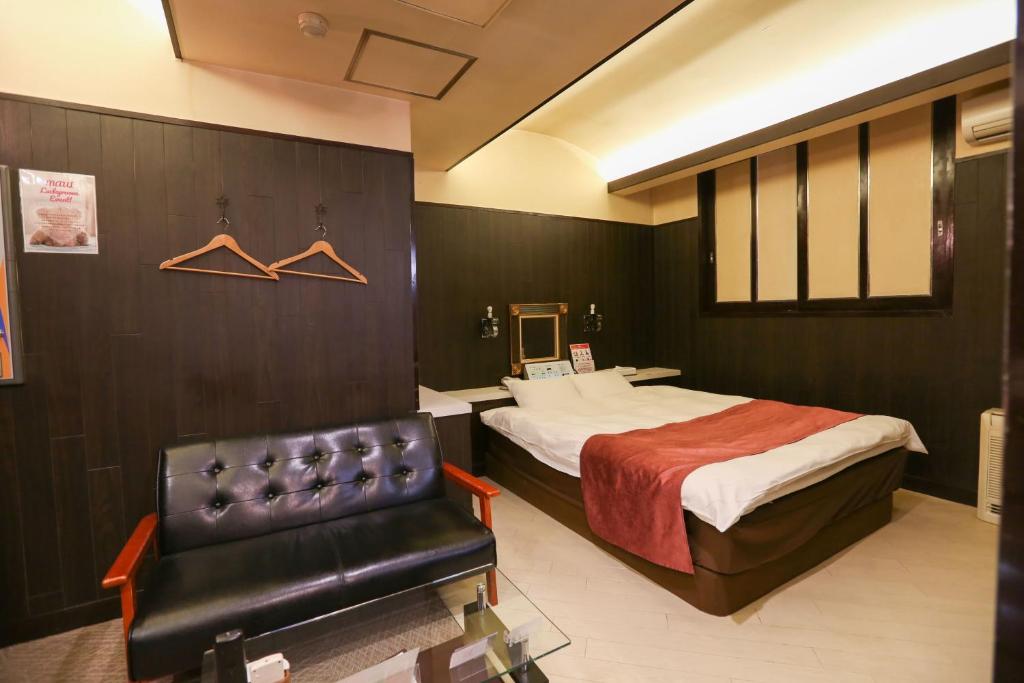 une chambre d'hôtel avec un lit et un fauteuil en cuir dans l'établissement ホテルロコズマウイ, à Honjo