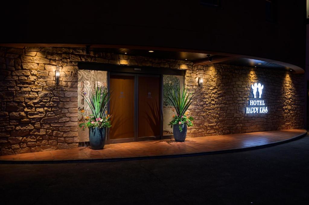 un bâtiment avec deux plantes en pot devant une porte dans l'établissement ハッピーキス双葉店, à Kai