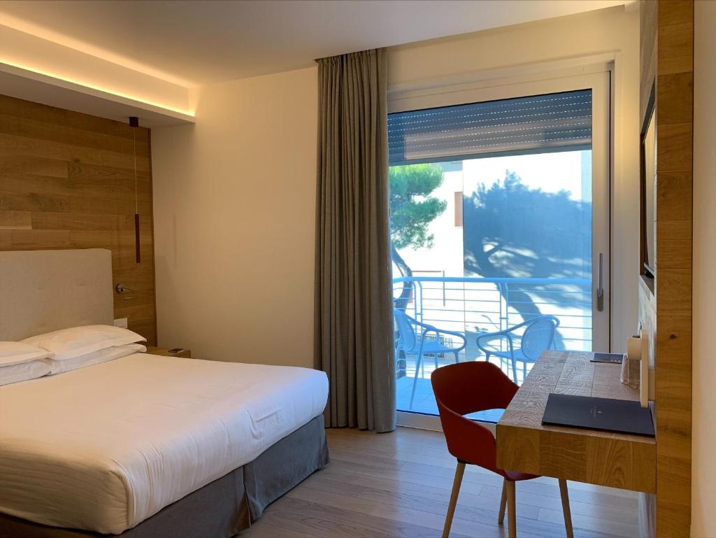 Cette chambre comprend un lit, un bureau et un balcon. dans l'établissement The Green Park Hotel WellnessSpa & Restaurant, à Cavallino-Treporti