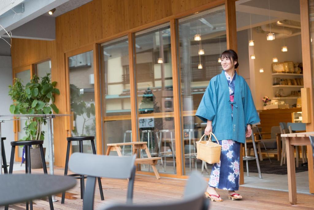 une femme debout devant une pièce avec des tables et des chaises dans l'établissement TSUCHIYA Kinosaki onsen, à Toyooka