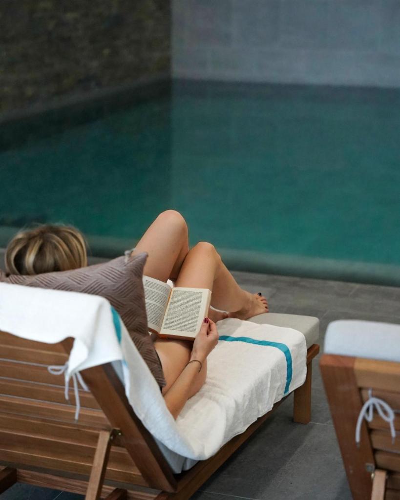 une femme dormant dans un lit avec un livre et une piscine dans l'établissement Résidence l'Ecrin d'Argent by My Mountain Resort, à Valmorel