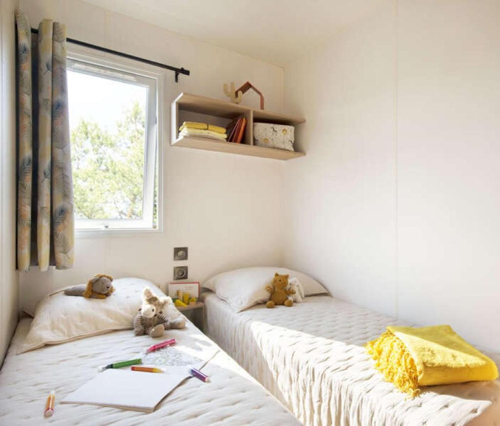 deux lits jumeaux dans une chambre avec fenêtre dans l'établissement Mobilhome 6 personnes climatisation, TV, lave-vaisselle, 2 salle de bain, 3 chambres au camping Les Vignes à Lit-et-Mixe dans les Landes avec piscine,, à Lit-et-Mixe 37 autres photos