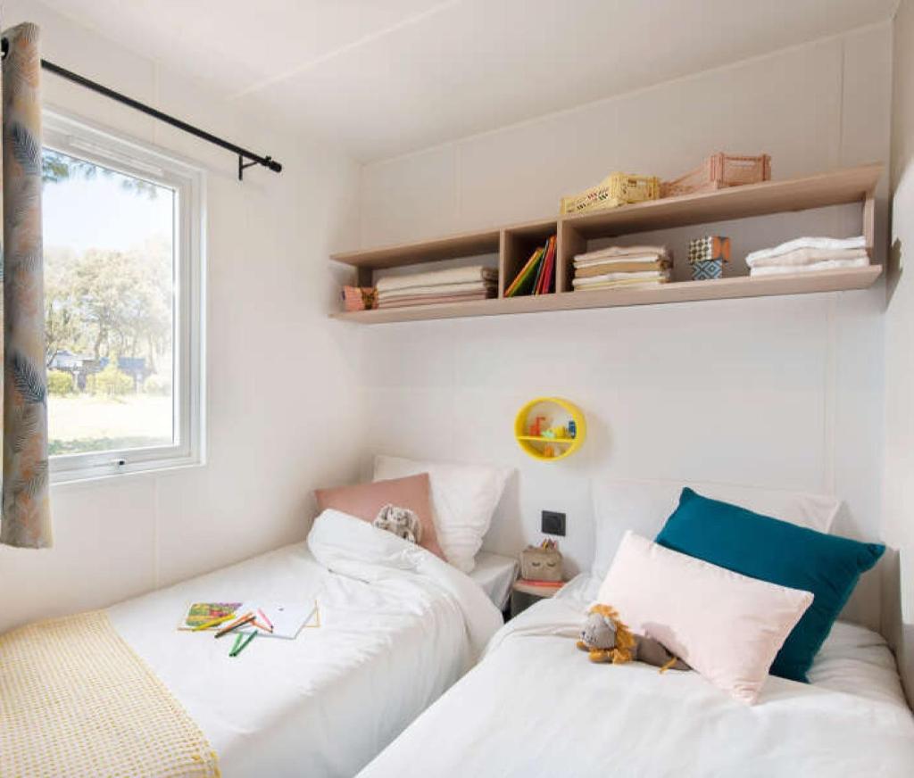 deux lits dans une petite pièce avec une fenêtre dans l'établissement Mobilhome 6 personnes climatisation, TV, lave-vaisselle, 2 salle de bain, 3 chambres au camping Les Vignes à Lit-et-Mixe dans les Landes avec piscine,, à Lit-et-Mixe