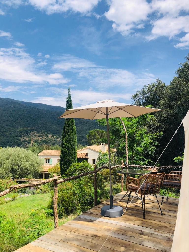 une terrasse en bois avec un parasol et des chaises. dans l'établissement glamping Bonheur, à Arles-sur-Tech