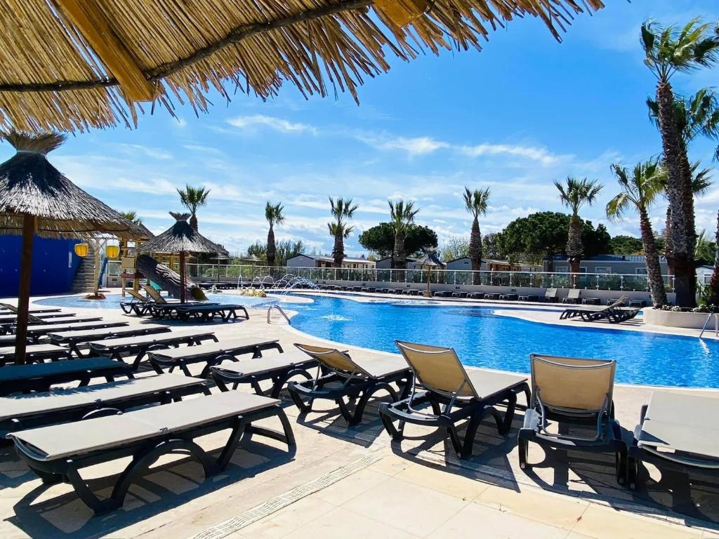 une piscine avec tables, chaises et palmiers dans l'établissement Mobil-home - Camping Le Marisol - Torreilles-plage, à Torreilles