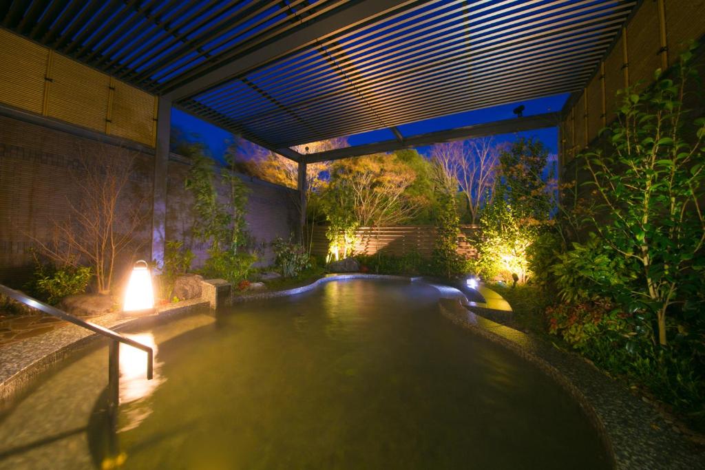 une piscine avec des lumières dans un jardin la nuit dans l'établissement Resorpia Beppu, à Beppu