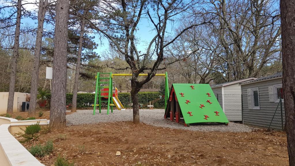 une aire de jeux avec un toboggan vert et un arbre dans l'établissement Camping Parc Saint Sauvayre, à Vagnas