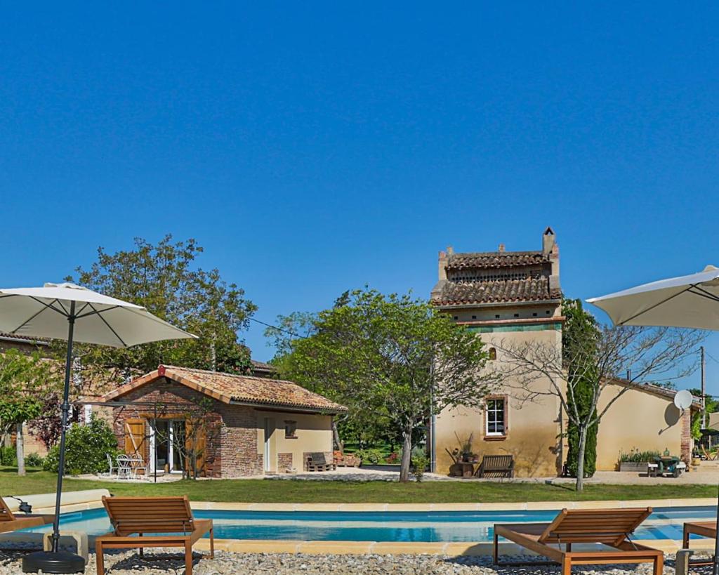 une piscine avec chaises et parasols devant un immeuble dans l'établissement Le Clos du Pīgeonnier - Gîte de charme, à Montauban