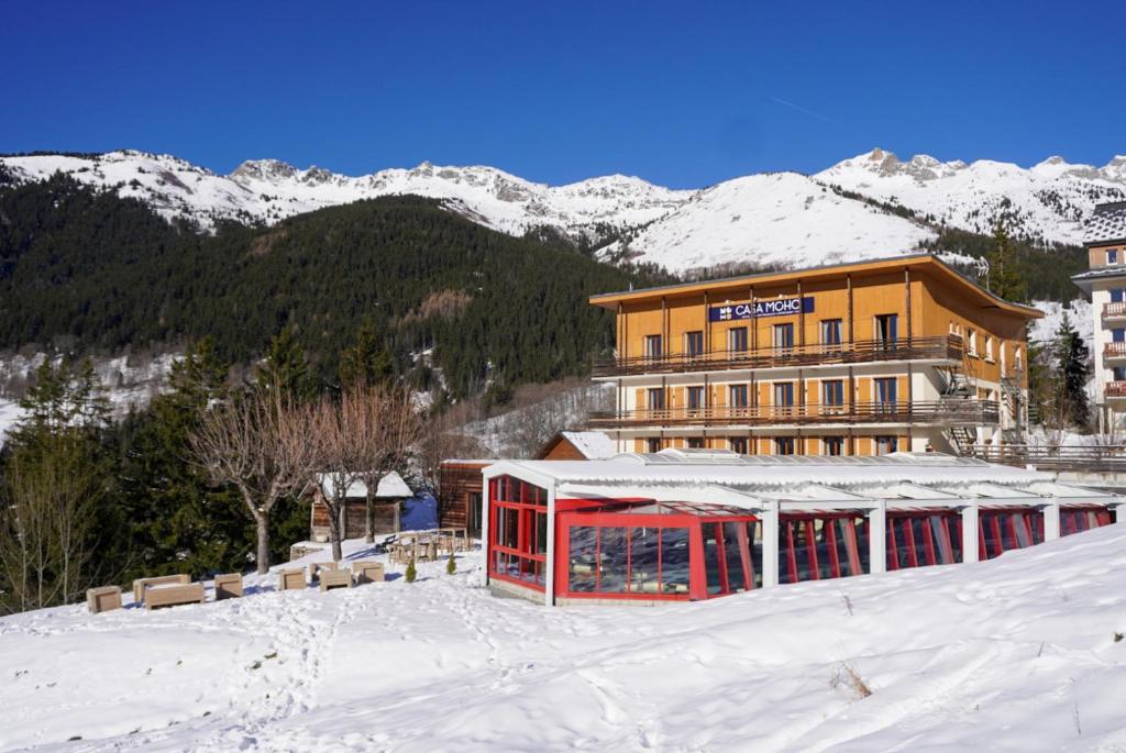 un hôtel sous la neige avec des montagnes en arrière-plan dans l'établissement Hôtel Casa Moho Saint-François-Longchamp 1450, à Saint-François-Longchamp