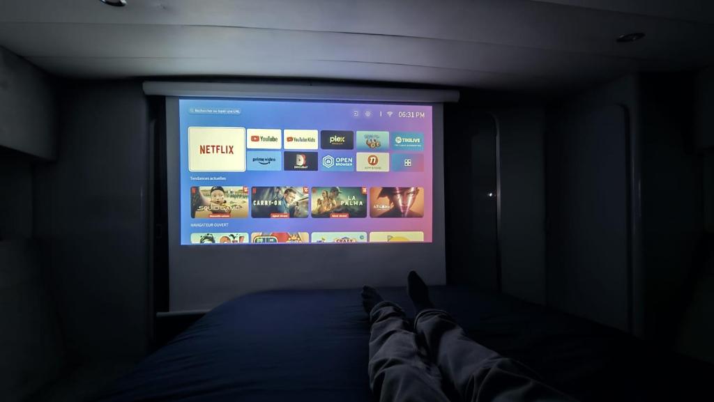 une personne regarde un écran de télévision dans une pièce sombre dans l'établissement Nuits insolites sur un bateau 12m en pleine nature, à Bully