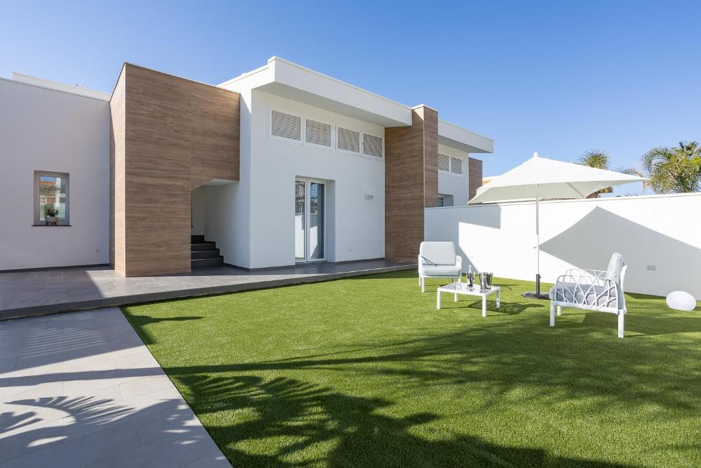 une maison dotée d'une pelouse avec deux chaises et un parasol dans l'établissement Villa Iside, à Marina di Ragusa