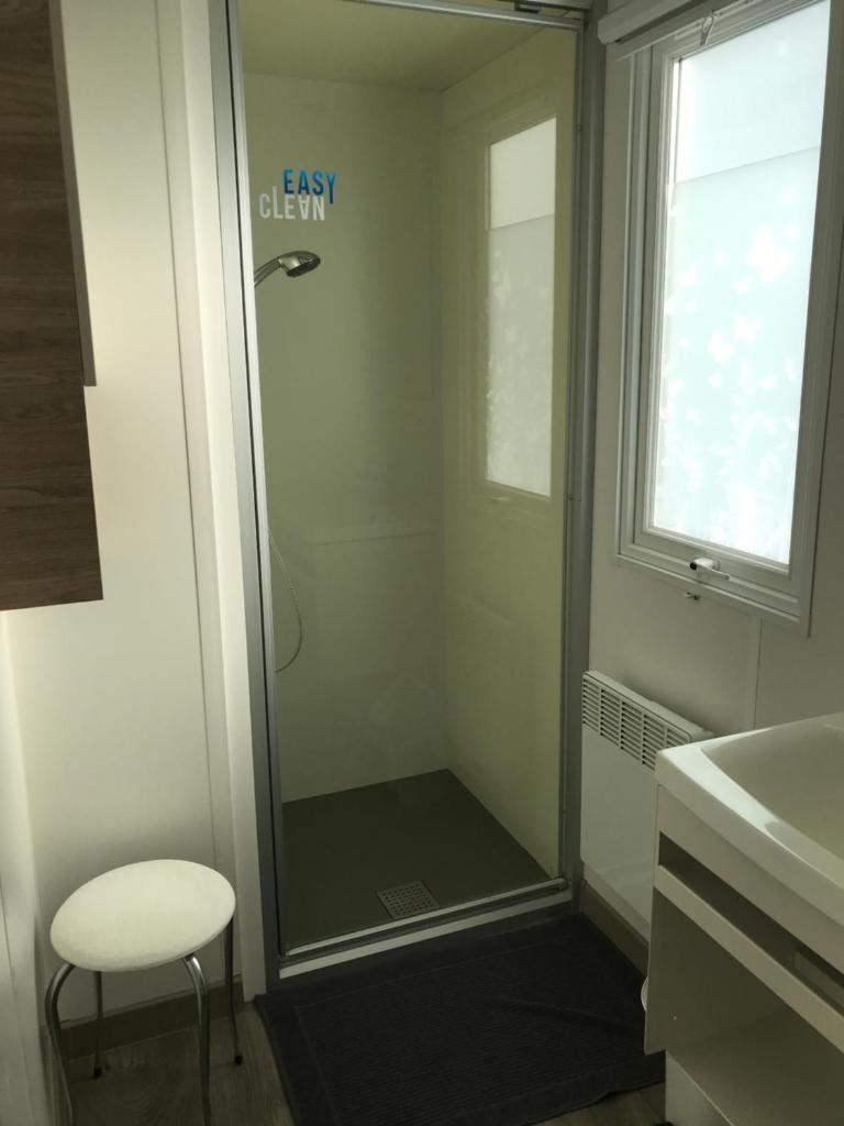 une douche avec une porte vitrée et un tabouret dans une salle de bain dans l'établissement MOBIL HOME 2 CHAMBRES 1 SDB - DOMAINE DE KERLANN, à Pont-Aven