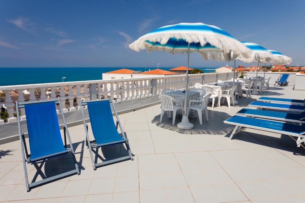 une terrasse avec des chaises, des tables et un parasol dans l'établissement HG Hotel Il Settebello, à Marina di Cecina