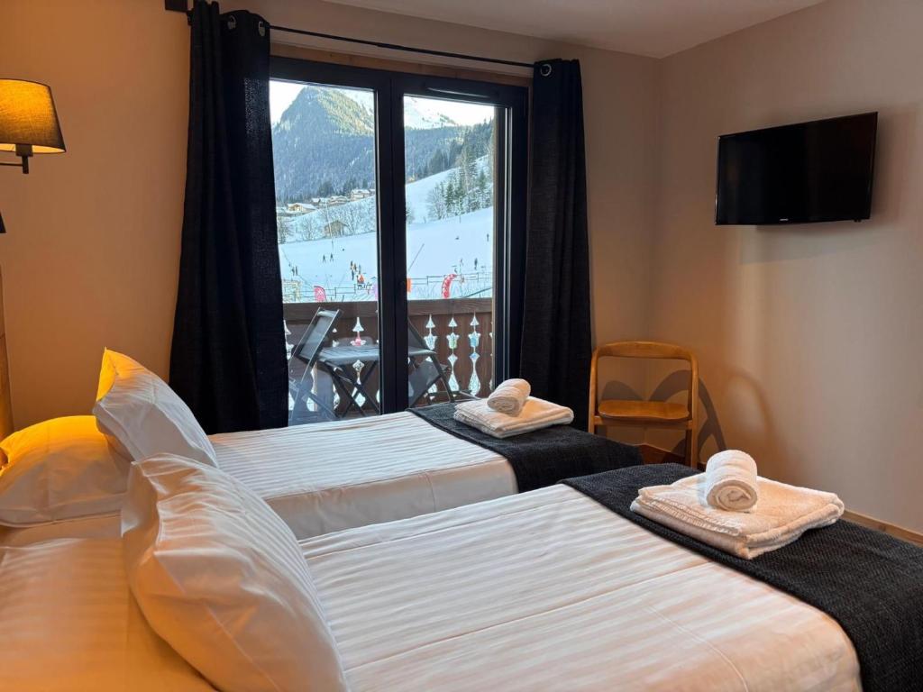 deux lits dans une chambre avec une grande fenêtre dans l'établissement Résidence Frond'Neige, à Morzine