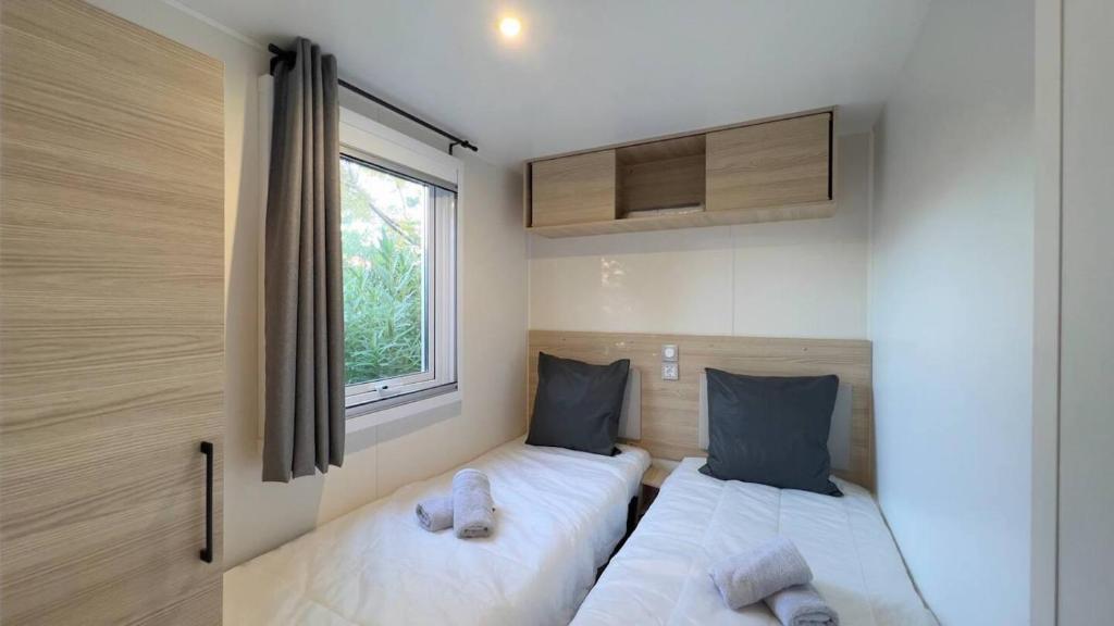 deux lits dans une petite pièce avec une fenêtre dans l'établissement Mobil-Home Les Lauriers Roses Camping Siblu 4****, à Fréjus
