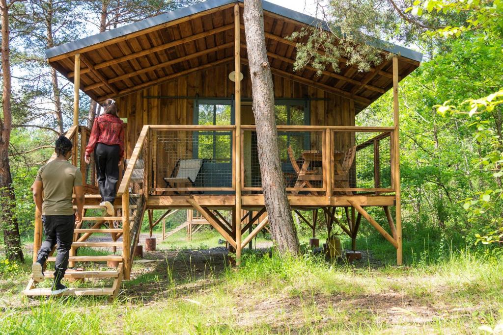 Deux personnes montent les escaliers jusqu'à une cabane dans les arbres. dans l'établissement Camping L'Ondine de Provence, à La Motte-Chalançon